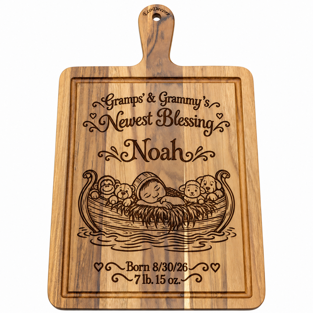 A rectangular wooden cutting board with a rounded handle, featuring engraved text reading 'Gramps & Grandma's Newest Blessing Noah' and a baby in a boat with teddy bears, plus birth details. The board is shown on a plain white background.